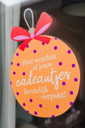Sfeerbeeld Raamsticker 37x50cm, oranje kerstbal met tekst “Hier worden cadeautjes feestelijk verpakt!”, raamdecoratie Kerst, feestelijke raamstickers voor winkels